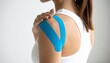 © Abdul Rosid - wearing a white sleeveless top with blue kinesiology tape applied to her right shoulder. He holds his injured shoulder, indicating pain or discomfortn