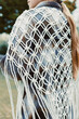 © DSMT - Person wears a handcrafted macrame shawl made of white cord while standing outside on a sunny day in a park setting