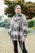 © DSMT - Woman stands in park wearing knitted outerwear. She looks to the side as trees and buildings surround her during cloudy weather