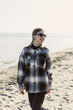 © DSMT - Woman walks along the beach wearing sunglasses and a checkered jacket while smiling in the sunlight