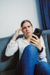 © DSMT - Woman sitting on a couch checking her phone while showing signs of concern or worry in a room with soft lighting