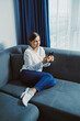 © DSMT - Woman sits on sofa and uses smartphone while relaxing in living room during daytime