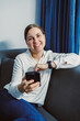 © DSMT - Woman sitting on a couch using a smartphone while smiling in a cozy indoor setting with blue curtains and natural light during the day