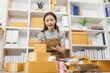 © Pattra - A woman is sitting on the floor in front of a stack of boxes. She is smiling and looking at her laptop. The scene suggests that she is working or studying, possibly for a business or school project