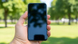 © Photography - Hand holding smartphone with blank screen outdoors in park with green grass and trees in background on sunny day for technology and communication concept with mobile and nature with device