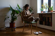 © DimaBerlin - Introverted teenager spending time alone at home, reading news in internet, scrolling social networks, messaging in smartphone. Teen girl sitting in cozy room with houseplants drinking cup of tea