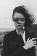 © SHOTPRIME STUDIO - Outdoor shot of a woman in a windy setting, wearing a dark coat, moody expression, monochrome tones, raw natural textures
