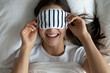 © fizkes - Healthy sleep care. Top view head shot portrait laughing young woman relax on cozy bedding put on terry sleeping mask enjoy bedtime early wakeup in cheerful playful mood start day with positive energy