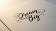 © Nataly - Dream Big motivational quote in black calligraphy on textured paper. Inspirational message with copy space