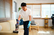 © Stella 16 - Man Wear blue gloves cleaning sofa upholstery at home using a powerful handheld vacuum cleaner