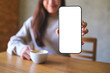 © Farknot Architect - Mockup image of a woman holding and showing a mobile phone with blank white screen while drinking cafe