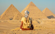 © denklim - Person sitting on sand looking at the pyramids in Giza plateau during sunset