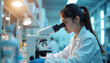© Vadym - Female scientist studies sample using microscope in lab. Woman in white coat conducts research. Lab worker is focused on examination process. Biotechnology medical tech concept is.
