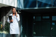 © Lumos sp - Portrait of a female woman doctor or nurse and  health care worker using a smartphone mobile phone  in front of hospital or clinic outside