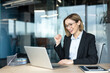 © Liubomir - Young businesswoman triumphantly cheering and clenching her fist while looking at a laptop in a contemporary office setting, experiencing achievement and good news online
