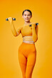 © SHOTPRIME STUDIO - Young athletic woman in matching orange fitness set lifting small dumbbells in a bright studio, confident posture, toned silhouette, modern activewear, energetic mood.