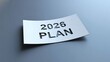 © TAIFUR - White paper with '2026 PLAN' cut out, casting shadow on a cool gray background, representing future planning and strategy.
