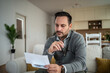 © Migma_Agency - Man evaluating finances at home reading letter feeling stressed
