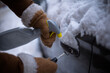 © Alliance - A gloved hand holds a car key while spraying a de-icer liquid into a frozen lock on a snow-covered vehicle to restore access.