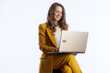 © Alliance - A businesswoman in a yellow suit laughs genuinely while interacting with her gold laptop, expressing happiness and satisfaction in her professional life.