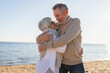 © Юлия Завалишина - Senior mature couple hugging enjoying outdoor recreation walking on beach. Old husband wife embracing with tenderness love enjoying sweet bonding. Grandmother grandfather together. Family moment love