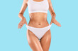 © Prostock-studio - Close up shot of unrecognizable fit woman wearing lingerie pulling up white panties standing isolated on blue studio background. Torso of slim female with flat belly in underwear top bra