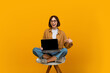 © Prostock-studio - Check this website. Happy woman pointing finger at laptop with black blank screen, sitting on chair and showing device with empty free space for mockup, yellow background
