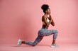 © miss irine - Sportive black woman makes stretching exercise. Athletic female practices yoga pose. Young girl does fitness workout routine on pink backdrop. Strong sportswoman trains body, keeps fit, stays healthy.