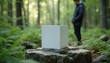 © miss irine - White cube stands on stone in forest. Man walks on trail in background. Modern product presentation. Geometric art object in nature. Promo display for eco lifestyle brand outdoor.