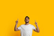 © Prostock-studio - Cheerful millennial arab guy in white t-shirt pointing up with both hands at copy space for advertisement or text and smiling, young middle eastern man posing on yellow studio background