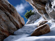 © Milos - An intimate view of a rocky pathway winding through a snow-covered landscape, surrounded by towering rock formations and scattered greenery, inviting exploration and adventure.