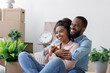 © Prostock-studio - Satisfied young black husband and wife hugging, sit on floor with cardboard boxes, things and plants in new flat, free space. Happy couple enjoying result of renovation, rest after moving, relocation