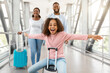 © Prostock-studio - Modern Travels. Portrait of excited African American girl having fun, sitting on baggage, riding suitcase and spreading arms, pretending air plane flying, playing in airport terminal