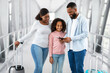 © Prostock-studio - Portrait Of Cheerful Black Family Of Three People Standing Indoors In Modern Airport Terminal With Baggage, Dad Holding And Looking At Passports With Boarding Passes, Mom And Daughter Hugging