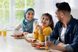 © Prostock-studio - Happy islamic family with little daughter eating tasty breakfast together in kitchen at home, joyful arab parents and cute female child enjoying delicious food and drinking orange juice, closeup