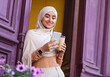 © Prostock-studio - Glad attractive millennial middle eastern woman in hijab chatting on phone and enjoying favorite drink near front door outdoor. Online call, social networks, surfing in internet and drink coffee