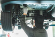 © buritora - A male car mechanic performing maintenance, inspection and work under a vehicle going up on a lift