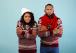 © Prostock-studio - Portrait of african american couple in Christmas sweaters, hat and scarf shivering, looking at camera on blue studio background. Cold winter weather