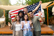 © Prostock-studio - Portrait of multiethnic millennial friends with American flag waving at camera and smiling, posing near RV at camping site. Group of diverse young people celebrating patriotic holiday together outdoor