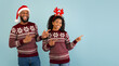 © Prostock-studio - Christmas sales. Excited african american couple pointing aside at empty space for your advertisement over blue background, panorama with copy space. Holiday offer and promo