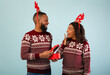 © Prostock-studio - Happy black man giving gift box to surprised wife and celebrating New Year or Christmas together over blue background. Happy african american spouses wearing deer horns