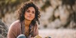 © Ketsaratchaya - Thoughtful young woman with curly hair enjoying a book outdoors near rocky landscape during a serene moment of reflection and connection to nature