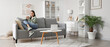 © Pixel-Shot - Young woman with cup of coffee sitting on grey sofa in living room