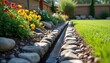 © Pete - Garden with installed French drain system. Channel drainage made of rocks and gravel. Flowerbed with flowers near lawn and backyard. Landscape design and water runoff solution.