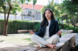 © crizzystudio - Young businesswoman meditating in outdoor park for stress relief