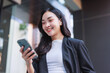© crizzystudio - Young asian woman smiling, enjoying smartphone and wireless earbuds