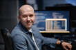 © Seventyfour - Portrait of middle aged Caucasian man smiling while sitting at desk in front of computer monitor displaying code, showing relaxed expression and looking into camera