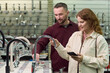 © pressmaster - Caucasian man and Caucasian young adult woman examining kitchen faucets in store showroom, woman holding smartphone while both inspecting fixtures on display