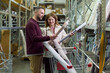 © pressmaster - Caucasian young adult man and Caucasian young adult woman standing in store aisle examining large rolls of wallpaper together, both holding products and looking at each other
