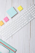 © Beti Argi - Vertical top view of a modern workspace with white keyboard, colorful sticky notes and green notebook on light wooden desk. Clean minimalist style with copy space. Concept of creative workspace